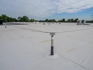 Flat white rooftop with a single vent post in the foreground and distant HVAC equipment under a blue sky.